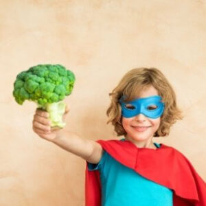 Kind im Supermann-Cape mit Brokkoli in der Hand.